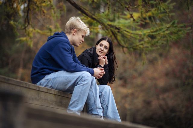 Kuvassa kaksi nuorta juttelee ulkona puistossa. Kuvassa toinen nuori kuuntelee keskittyneesti, mitä toinen kertoo.