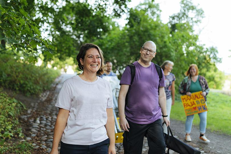 Iloinen ryhmä kävelee puistossa tapahtumatavaroita kantaen