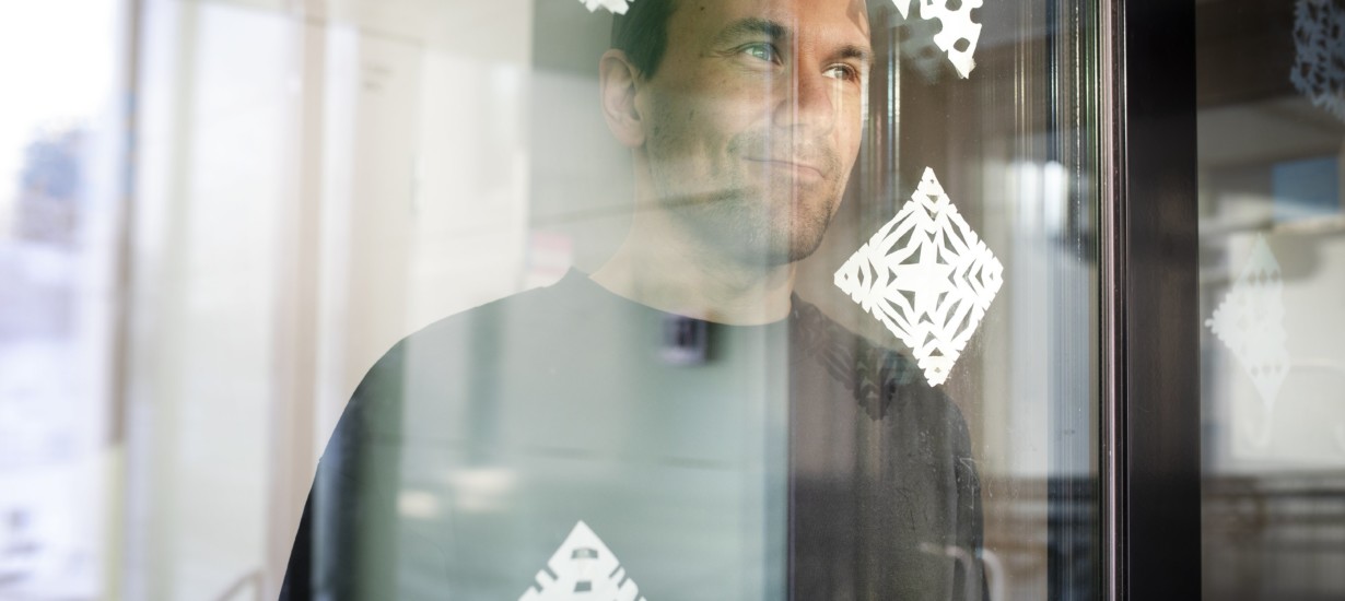 Teemu Oinola hymyilee ikkunan paperihiutaleilla koristellun ikkunan takaa