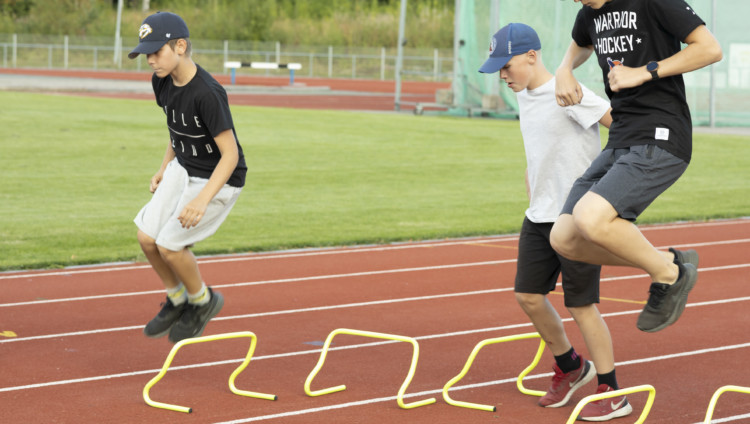 Nuoret hyppivät pikkuaitojen yli urheilukentällä