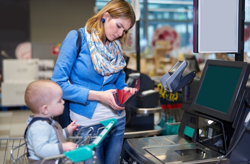 Pieni lapsi ostoskärryissä, lapsen äiti lompakko kädessä.