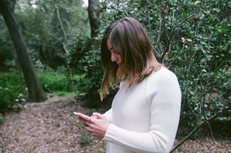 Nuori seisoo metsässä ja selaa puhelinta.