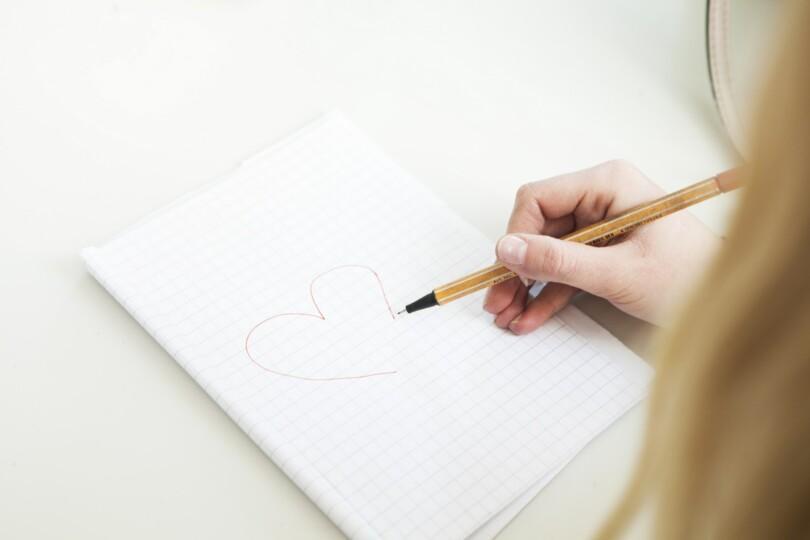 Tytön käsi piirtämässä sydäntä ruutupaperille