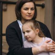 Vanhempi pitää lasta sylissään. Taustalla portaan kaide ja talon seinä, jossa ikkuna.