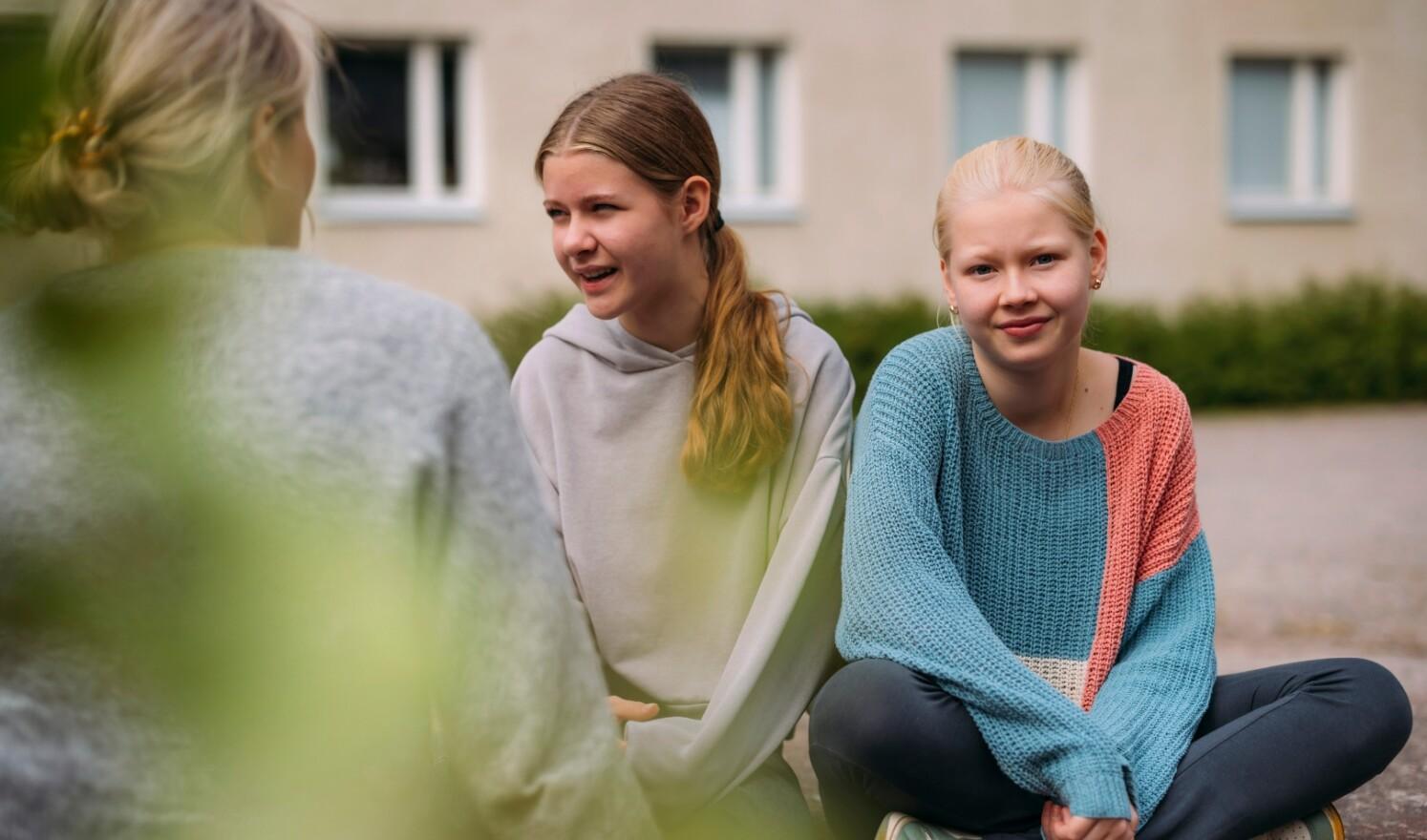 Kolme tyttöä istuskelee ulkona