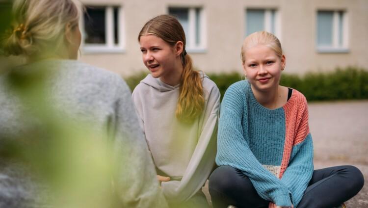 Kolme tyttöä istuskelee ulkona