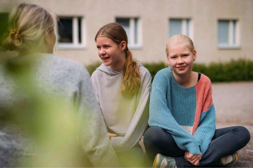 Kolme tyttöä istuskelee ulkona