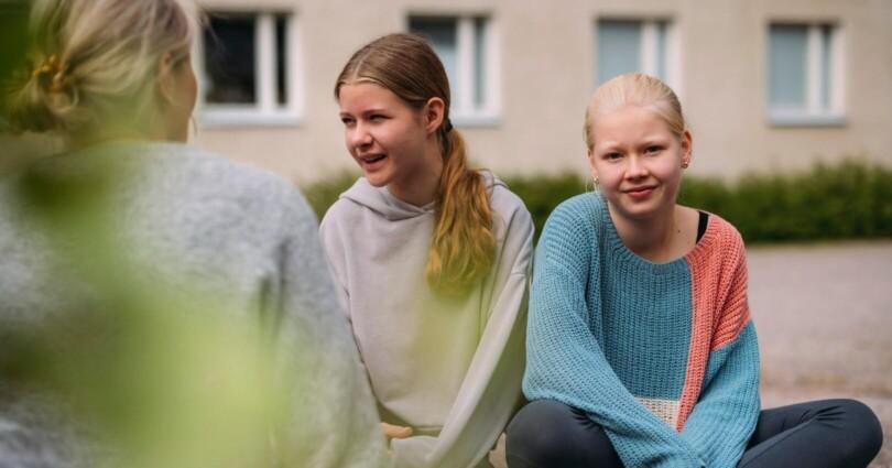 Kolme tyttöä istuskelee ulkona