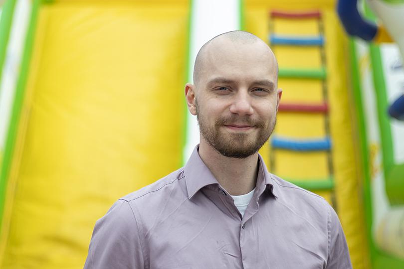 Kuvassa MIELI ry:n Jaakko Hiltunen katsoo kameraan neutraali ilme kasvoillaan. Taustalla keltainen kangas ja muoviset moniväriset tikkaat.