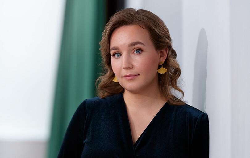 Kuvassa Julia Sangervo katsoo suoraan kameraan. Taustalla valkoinen seinä ja vihreä verho.
