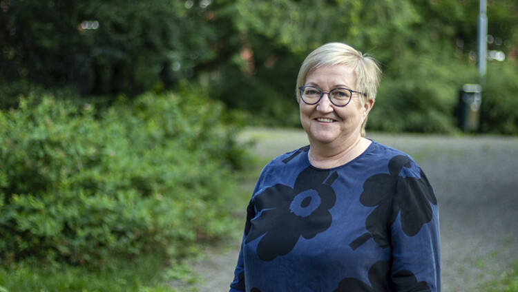 MIELI ry:n asiantuntija Sirkkaliisa Heimonen hymyilee ja katsoo suoraan kameraan ulkona puistossa.