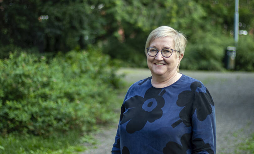 MIELI ry:n asiantuntija Sirkkaliisa Heimonen hymyilee ja katsoo suoraan kameraan ulkona puistossa.