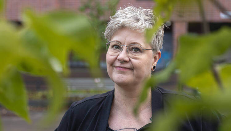 Kirjailija Raisa Omaheimo katsoo kuvassa suoraan kameraan. Vihreät lehdet reunustavat kuvaa. Kuva on otettu Länsi-Pasilassa Helsingissä.