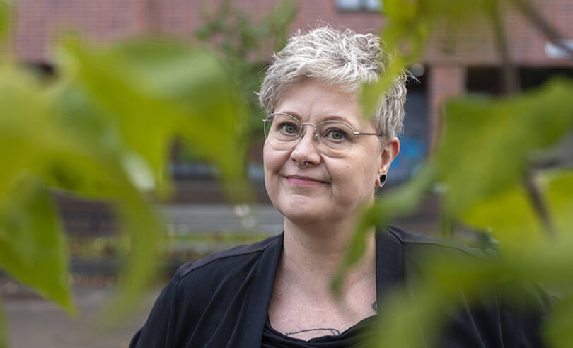 Kirjailija Raisa Omaheimo katsoo kuvassa suoraan kameraan. Vihreät lehdet reunustavat kuvaa. Kuva on otettu Länsi-Pasilassa Helsingissä.
