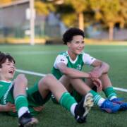 Nuoret jalkapallonpelaajan istuvat hymyillen nurmella.