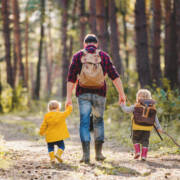 Isä kävelee kahden pienen lapsen kanssa metsätiellä.
