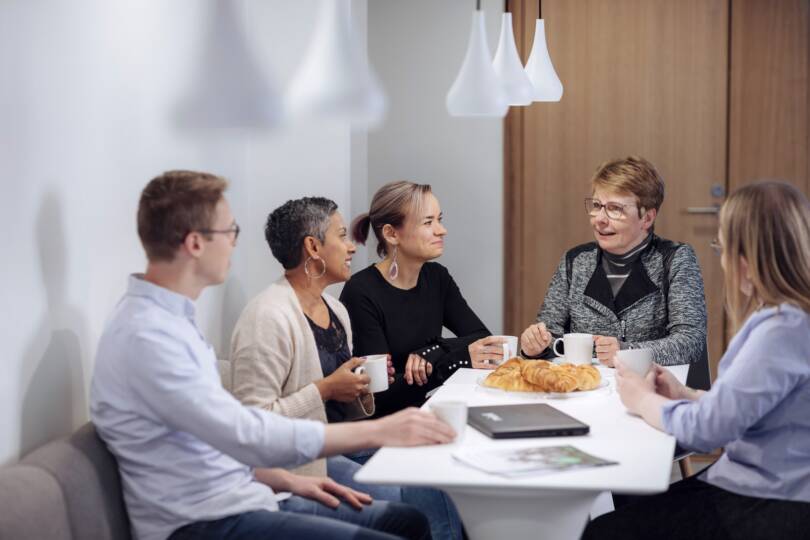 Työporukka juttelee kahvipöydän ääressä