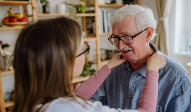 Naisoletettu takaapäin pitää käsiä valkohapsisen miehen hartioilla. Olisiko vaikapa hoitajan ja palvelutalon asiakkaan kohtaaminen?