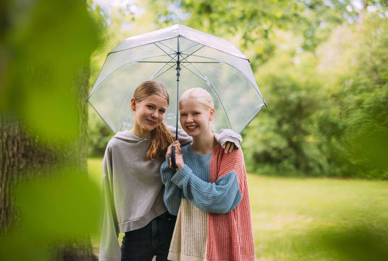 Kaksi nuorta seisoo sateenvarjon alla ja hymyilee